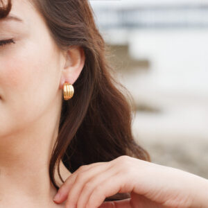 wide gold ribbed half hoop earrings worn on ear