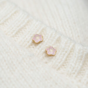 Pink glitter flower stud earrings styled on soft fabric background