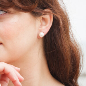gold button pearl stud earrings worn on the ear with a classic domed pearl shape