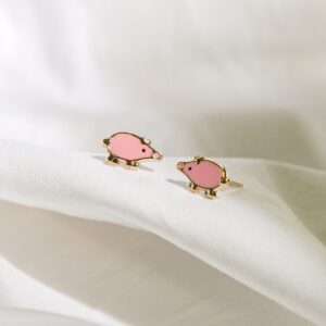 pink enamel pig stud earrings styled on soft white fabric