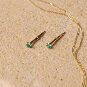 gold created emerald stud earrings styled on a warm stone surface with a gold chain